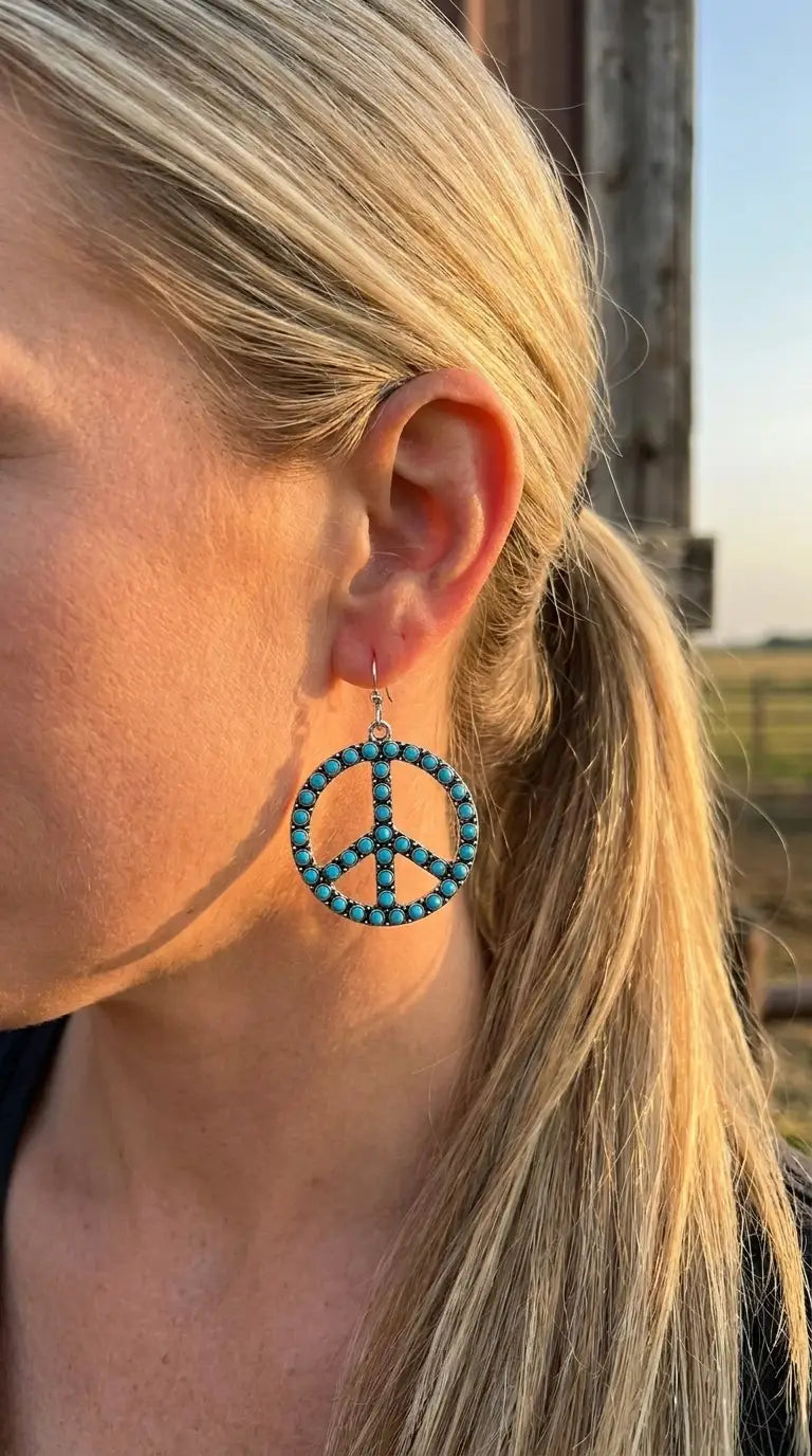 Close-up wearing the Cowhide & Conchos turquoise peace sign earrings — boho western detail up close.