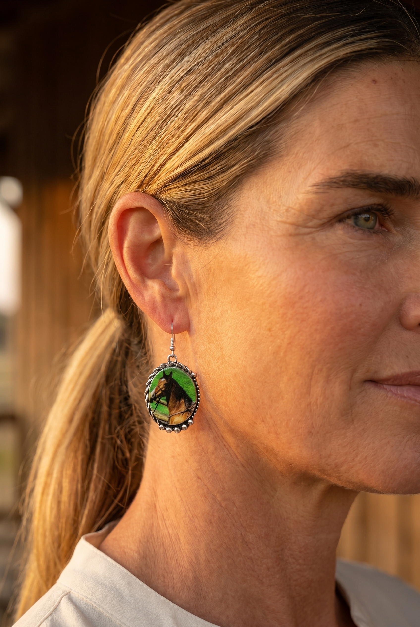 Ranch woman in golden-hour profile wearing the Cowhide & Conchos framed horse earrings — western ranch-life keepsake.