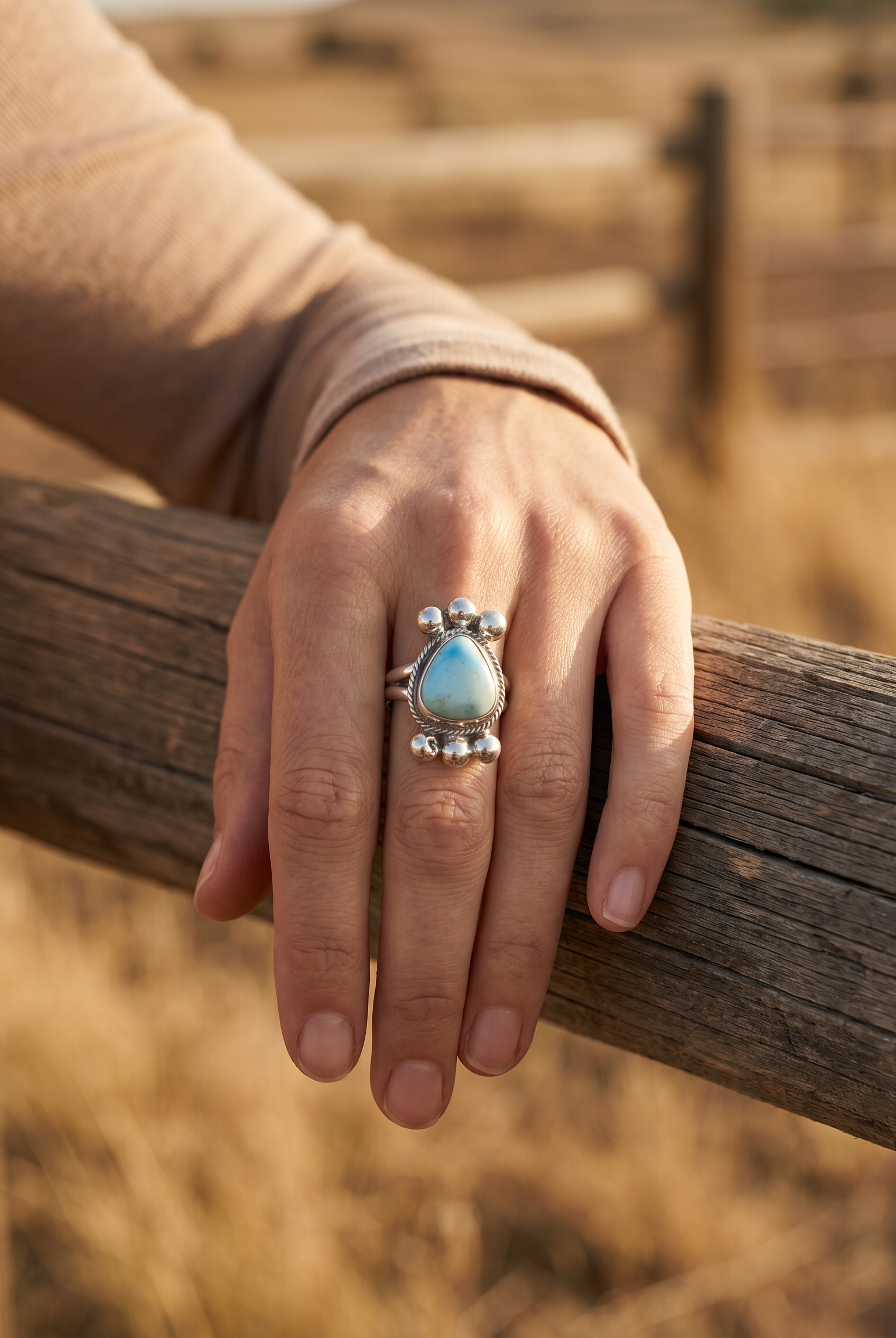 A hand on a ranch fence rail wearing the Cowhide & Conchos Joelias Draper Navajo Golden Hills turquoise ring — heirloom western style.