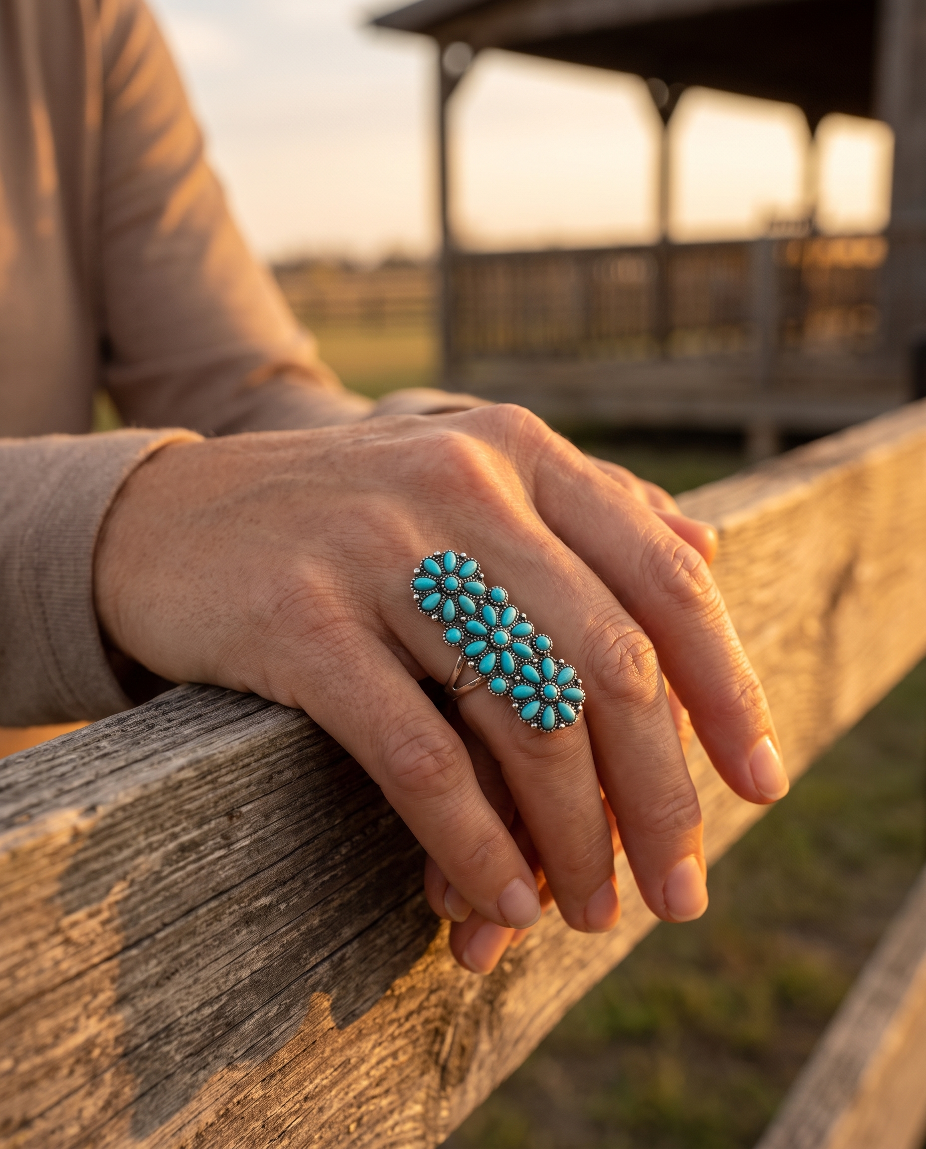 A hand on a ranch fence rail wearing the Cowhide & Conchos Western Desert Bloom faux-turquoise cluster ring — southwestern statement for less.