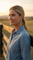 Golden-hour at the ranch fence wearing the Cowhide & Conchos 5-teardrop turquoise dangle earrings — bold western statement, easy to wear.