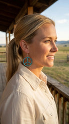 Golden-hour portrait wearing the Cowhide & Conchos turquoise peace sign earrings — free-spirited western style.