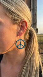 Close-up wearing the Cowhide & Conchos turquoise peace sign earrings — boho western detail up close.