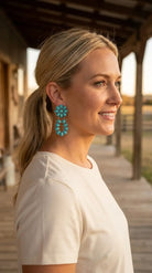 Ranch portrait wearing the Cowhide & Conchos turquoise cluster earrings — bold western statement, naturally worn.