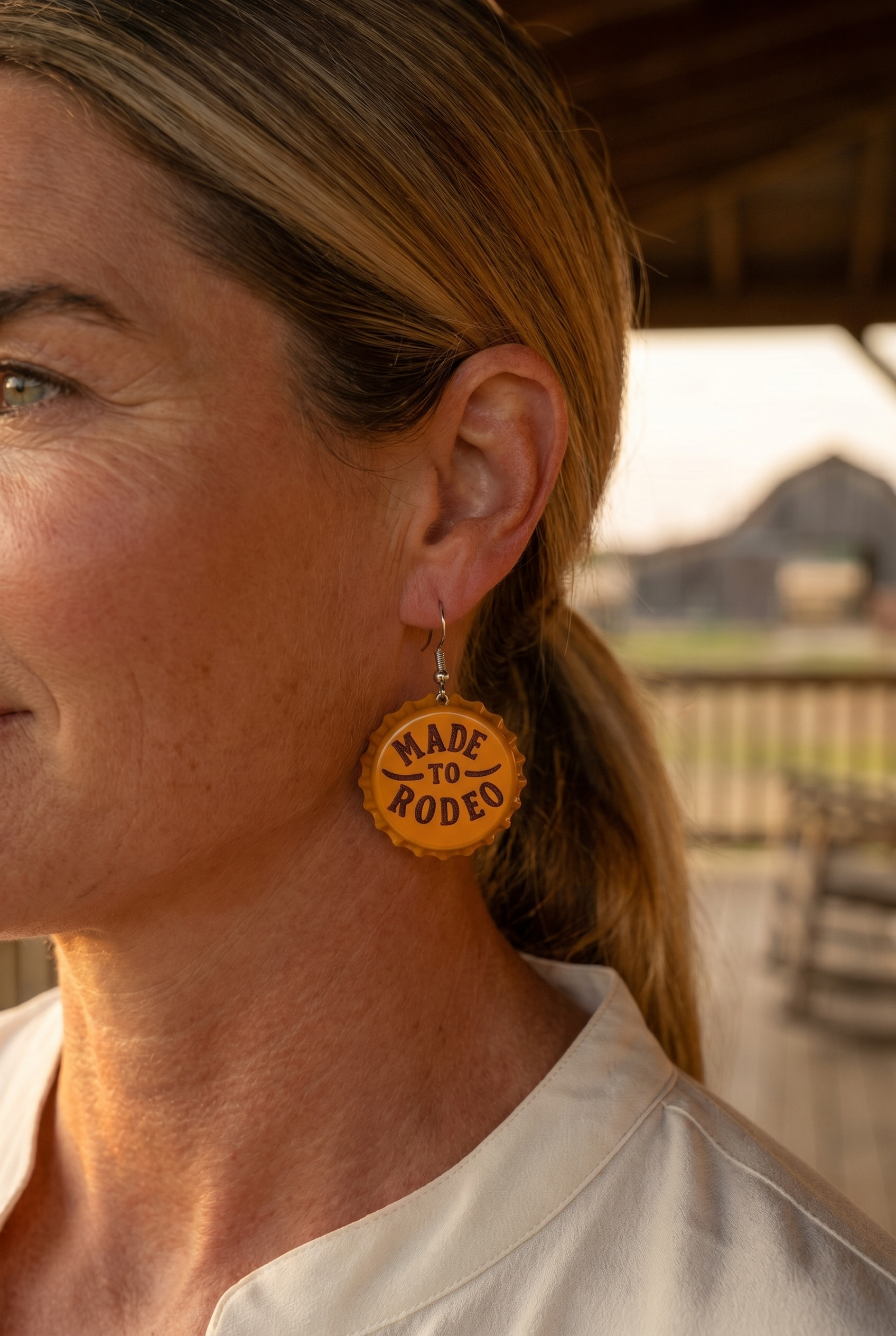 Ranch woman in golden-hour profile wearing the Cowhide & Conchos Made to Rodeo bottle-cap earrings — rodeo-ready western style.