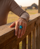 A hand on a ranch fence rail wearing the Cowhide & Conchos turquoise and sterling silver links ring — rugged western style.